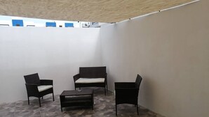 A small, enclosed patio area with a tiled floor, a sofa, two chairs, and a small table. - Acogedor departamento. (La Misión)