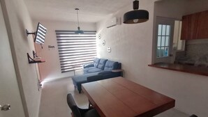 A modern living room with a sofa, a dining table, and a kitchen area with wooden cabinets. - Acogedor departamento. (La Misión)
