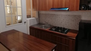 A compact kitchen with wooden cabinets, a stainless steel sink, and a gas stove. - Acogedor departamento. (La Misión)