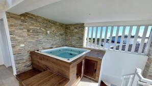 A spa area with a stone wall, wooden flooring, and a view of the sea through a balcony railing. - Unique lake, Golf & Jacuzzi in Hard Rock Golf PC (Punta Cana)