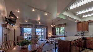 Uma cozinha espaçosa com armários de madeira, uma sala de jantar com mesa e cadeiras, e uma sala de estar com sofá e abajur.