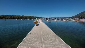 Um cais se estendendo sobre águas calmas, com barcos atracados por perto e uma colina arborizada ao fundo.