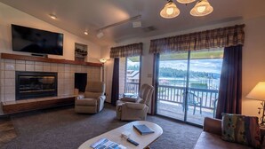 Uma sala de estar com lareira, televisão de tela plana, sofá e varanda com vista.