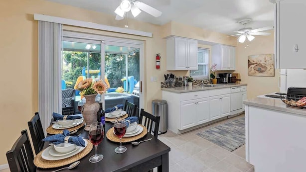 A modern kitchen with white cabinets, a dining area with a table set for two, and a large sliding glass door leading to a patio. - Cozy 4/3, Patio, King Bed, Bunk Room + Water Park! (Sanford)