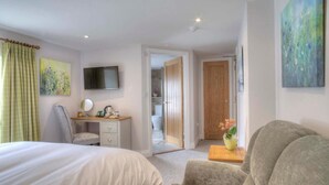 A hotel room with a bed, a desk with a chair, a television, and a door leading to a bathroom.