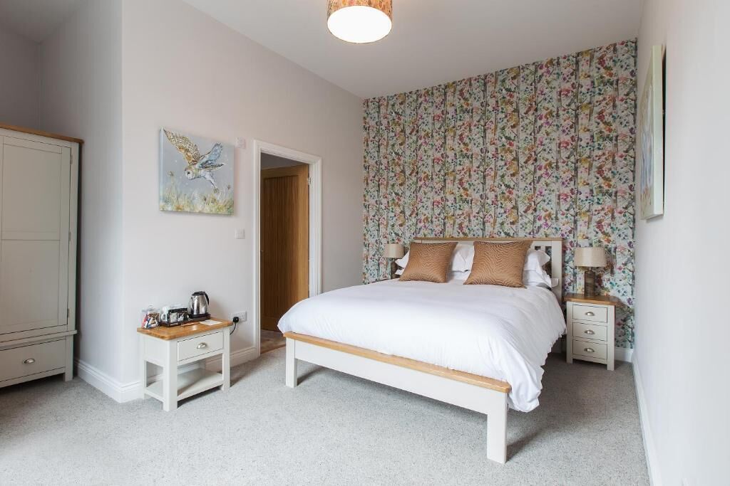 A bedroom with a bed, bedside tables, a nightstand, a wardrobe, and a floral wallpaper.