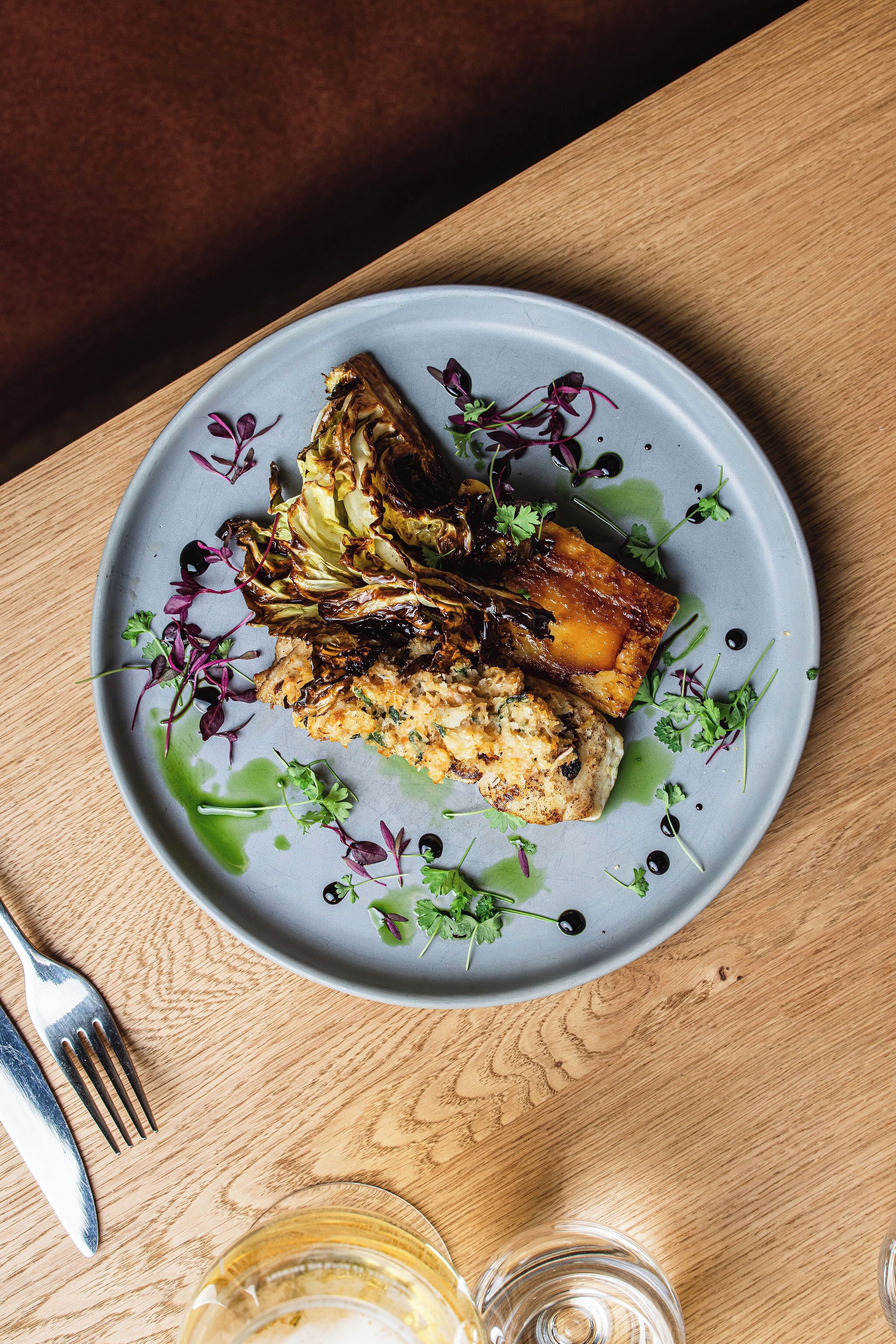 A plate of food on a wooden table with a fork and knife beside it.