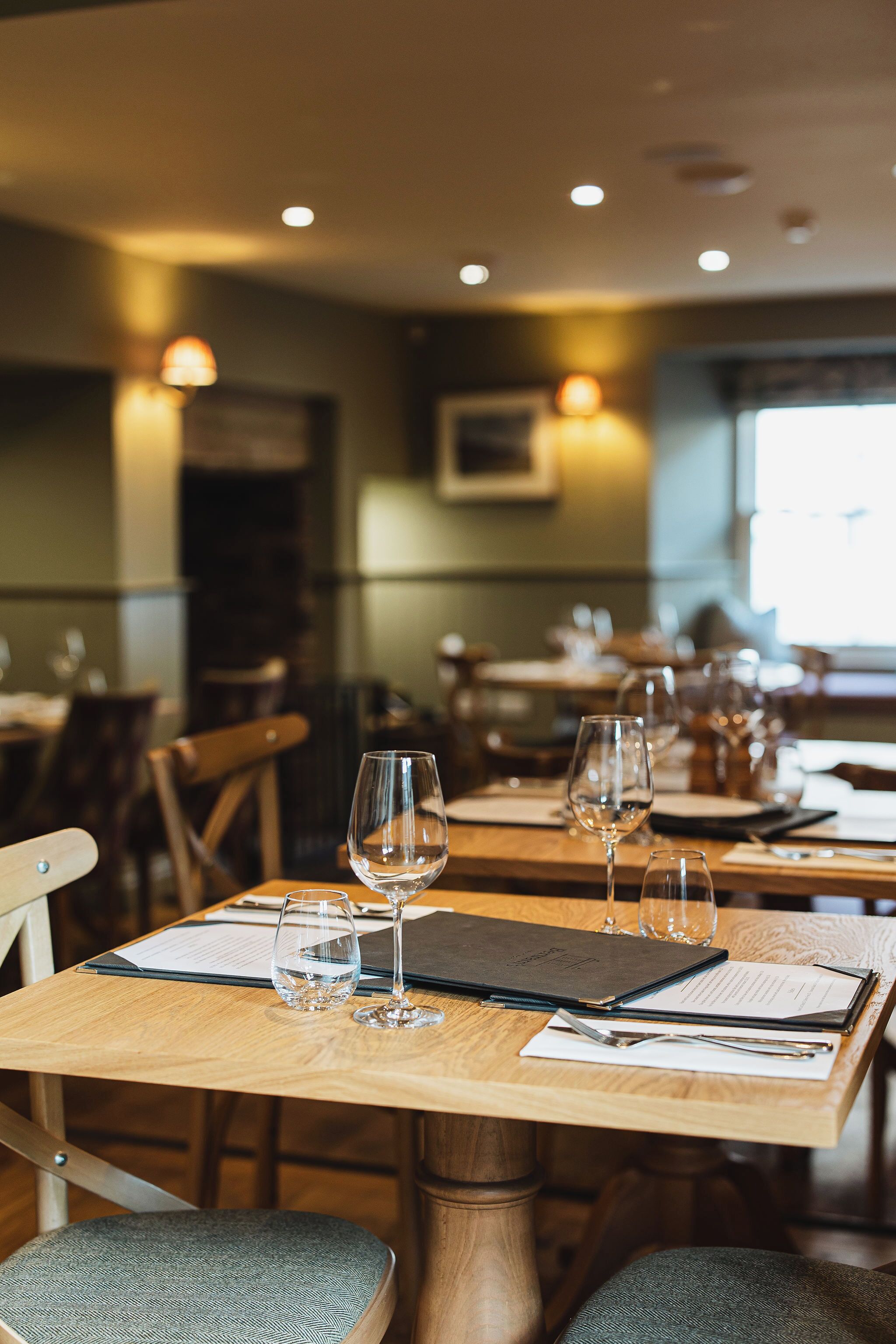 A restaurant interior with wooden tables, chairs, and wine glasses.