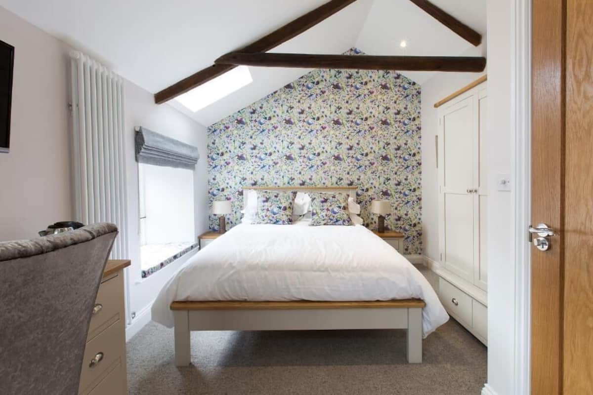 A bedroom with a bed, bedside tables, a window with blinds, a radiator, and a door.