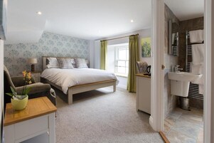 Un dormitorio con cama, mesita de noche, lámpara y vista al baño.