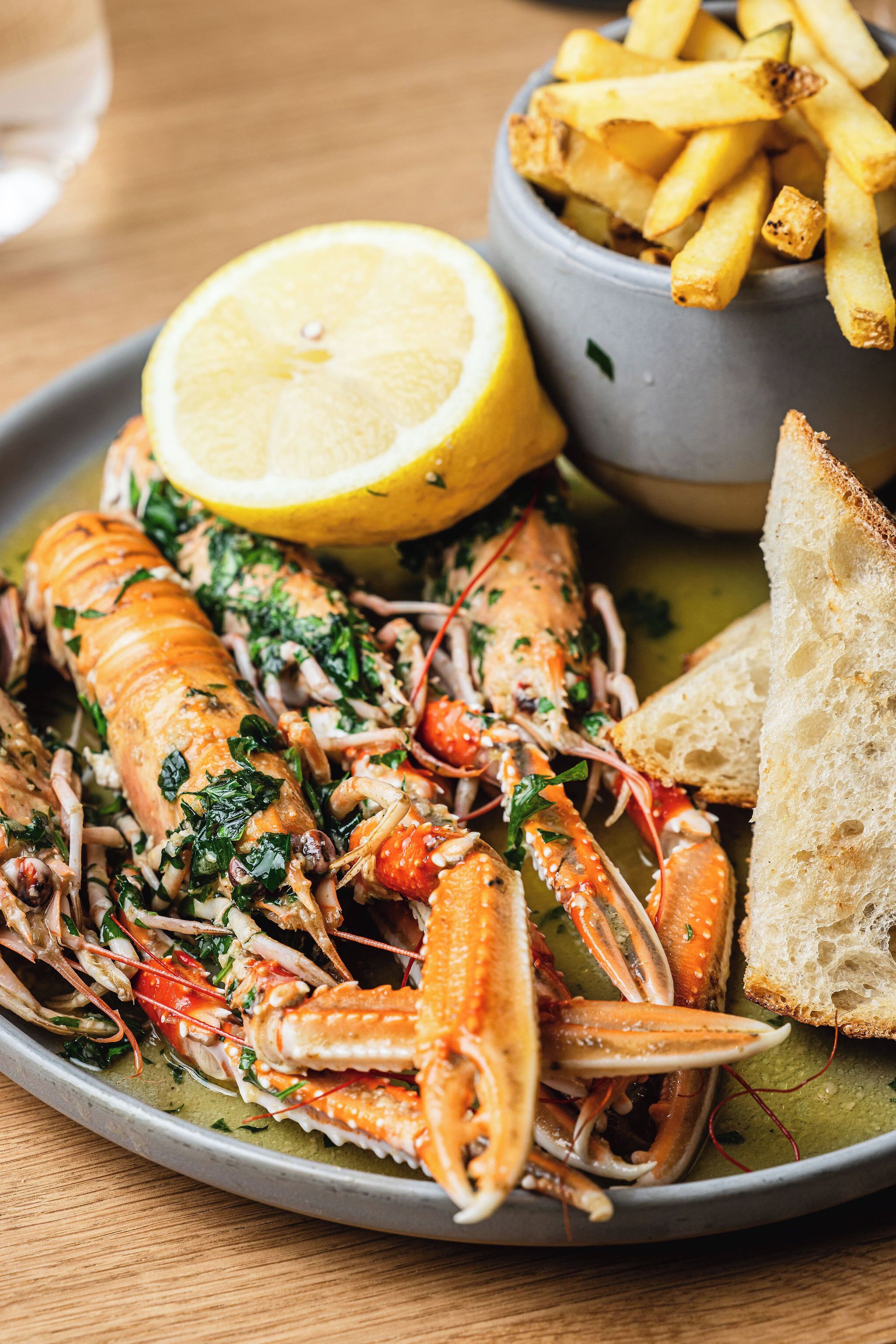 Une assiette de homard cuit, agrémenté d’herbes, de citron et accompagné de pain.