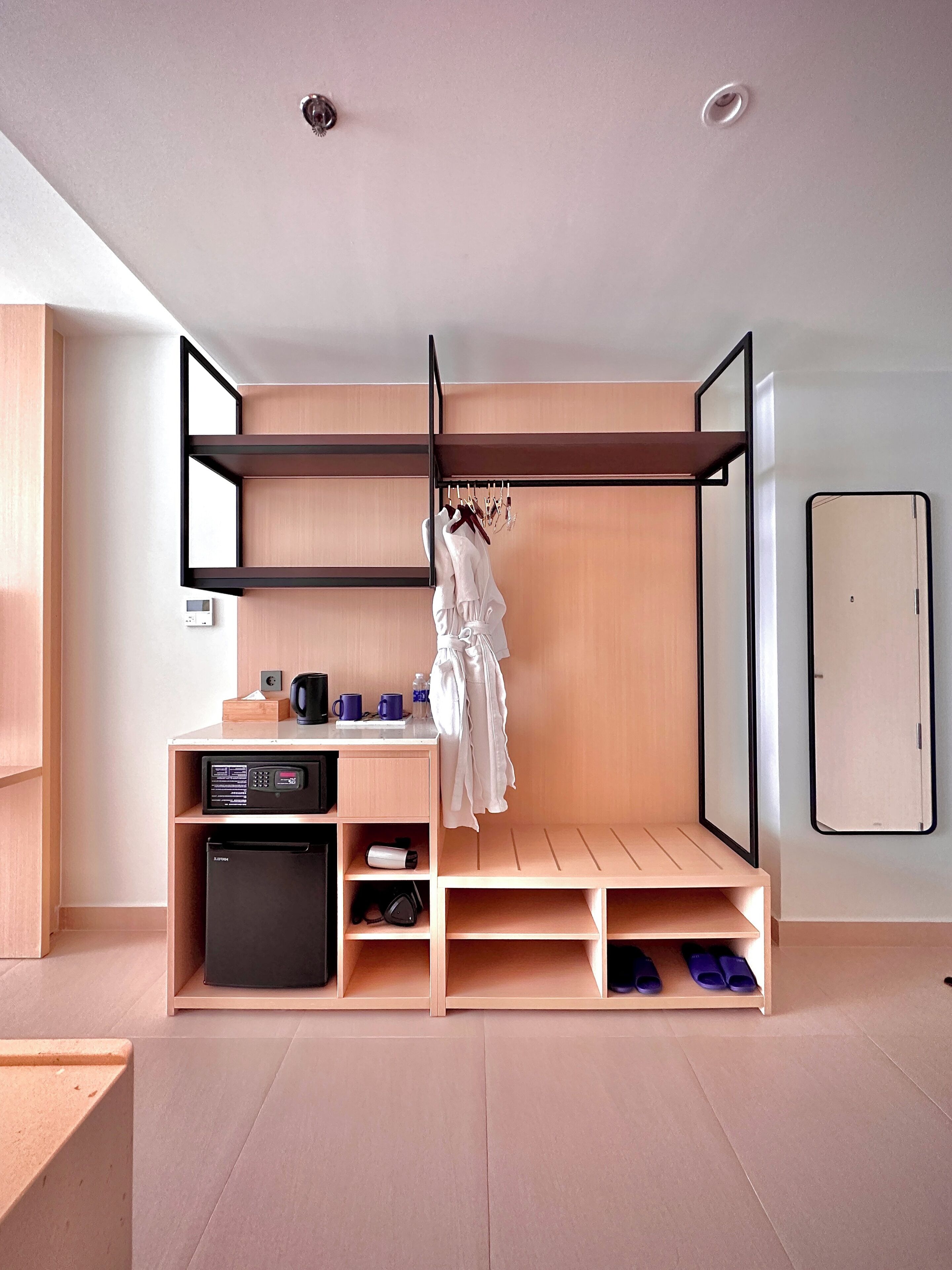 A compact, modern room with a built-in wardrobe, a small kitchenette, and a hanging clothes rack.