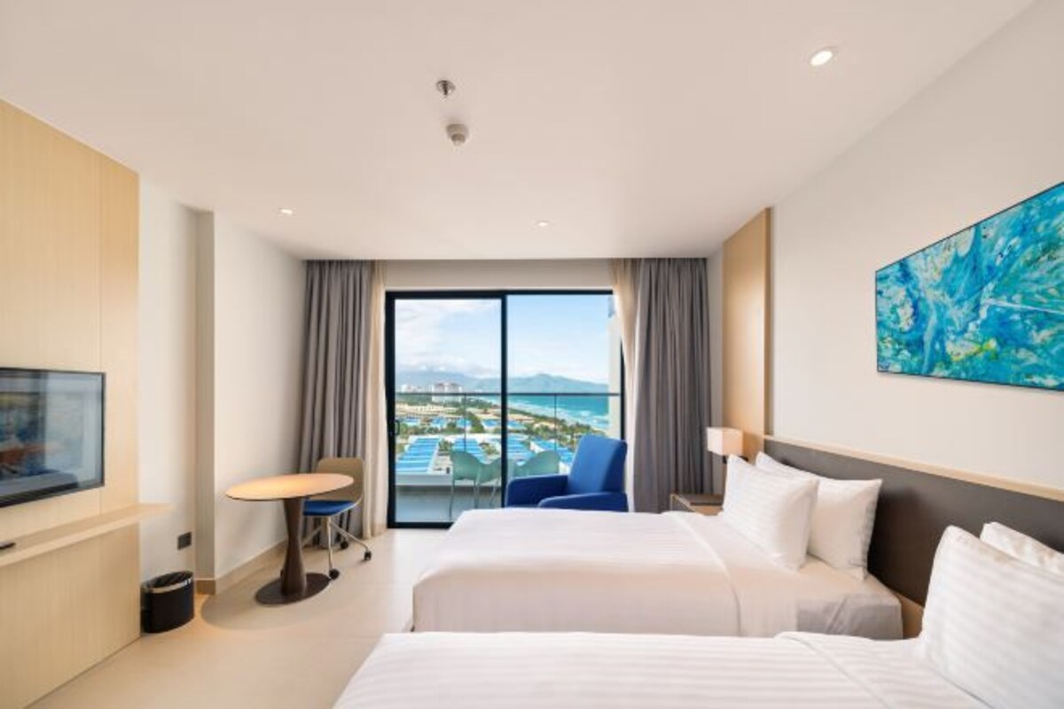 A hotel room with two beds, a TV, a desk, and a view of a pool and mountains.