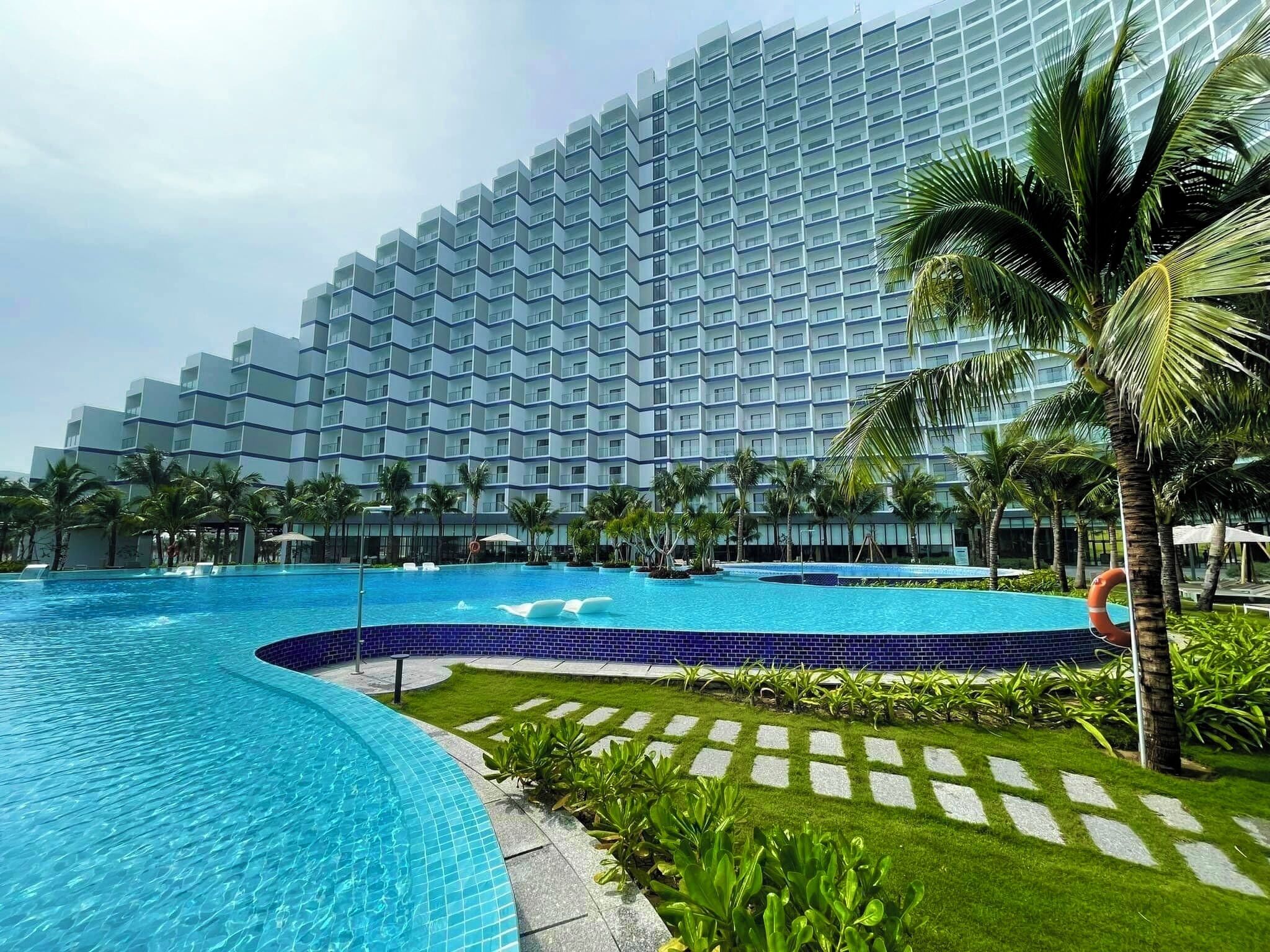 A modern hotel with a large pool area, surrounded by palm trees and a well-maintained lawn.