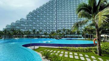 A modern hotel with a large pool area, surrounded by palm trees and a well-maintained lawn.