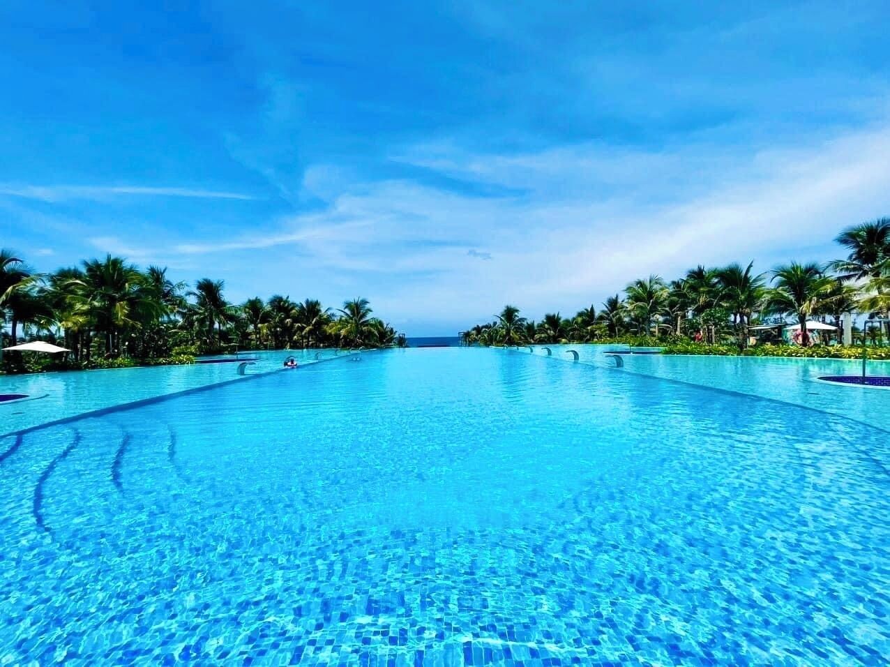 Une grande piscine d’un bleu éclatant, entourée de palmiers et bordée d’un ciel dégagé.