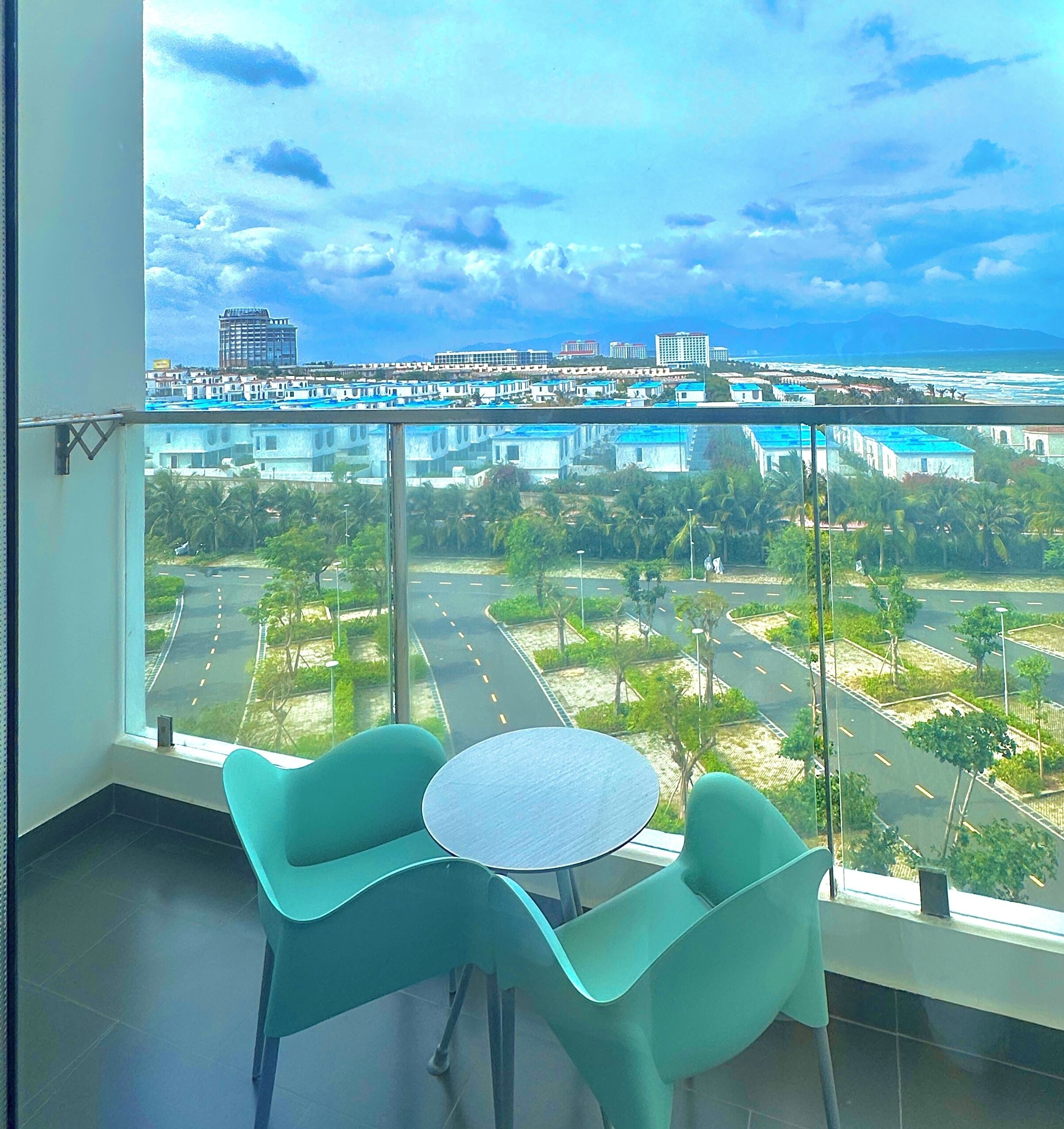 Ein Zimmer mit großem Fenster und Blick auf eine Küstenstadt, inklusive Straße, Grünflächen und Gebäuden.