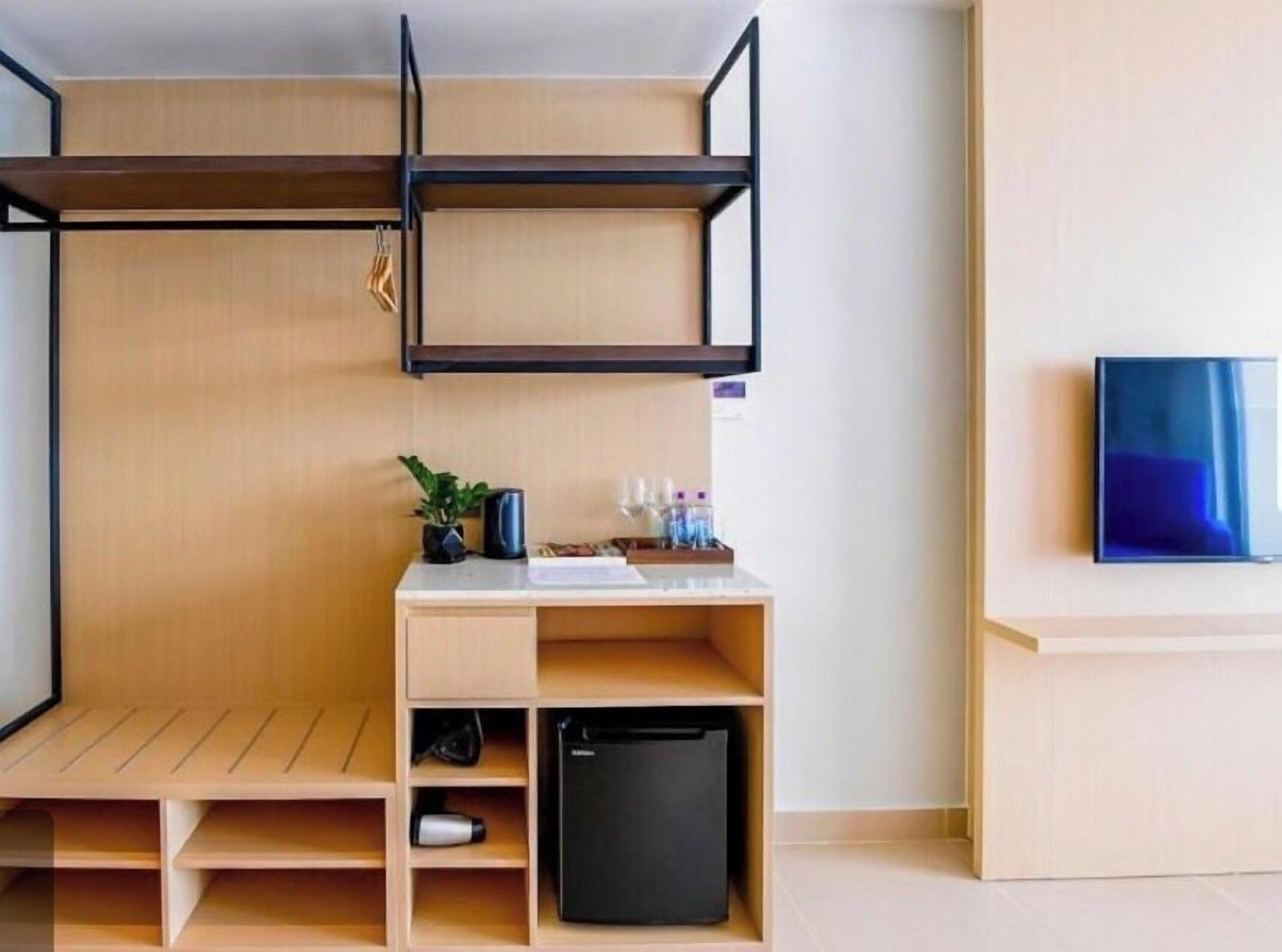 Una stanza compatta con un letto a castello, una scrivania con computer, un piccolo frigorifero e una TV a parete.