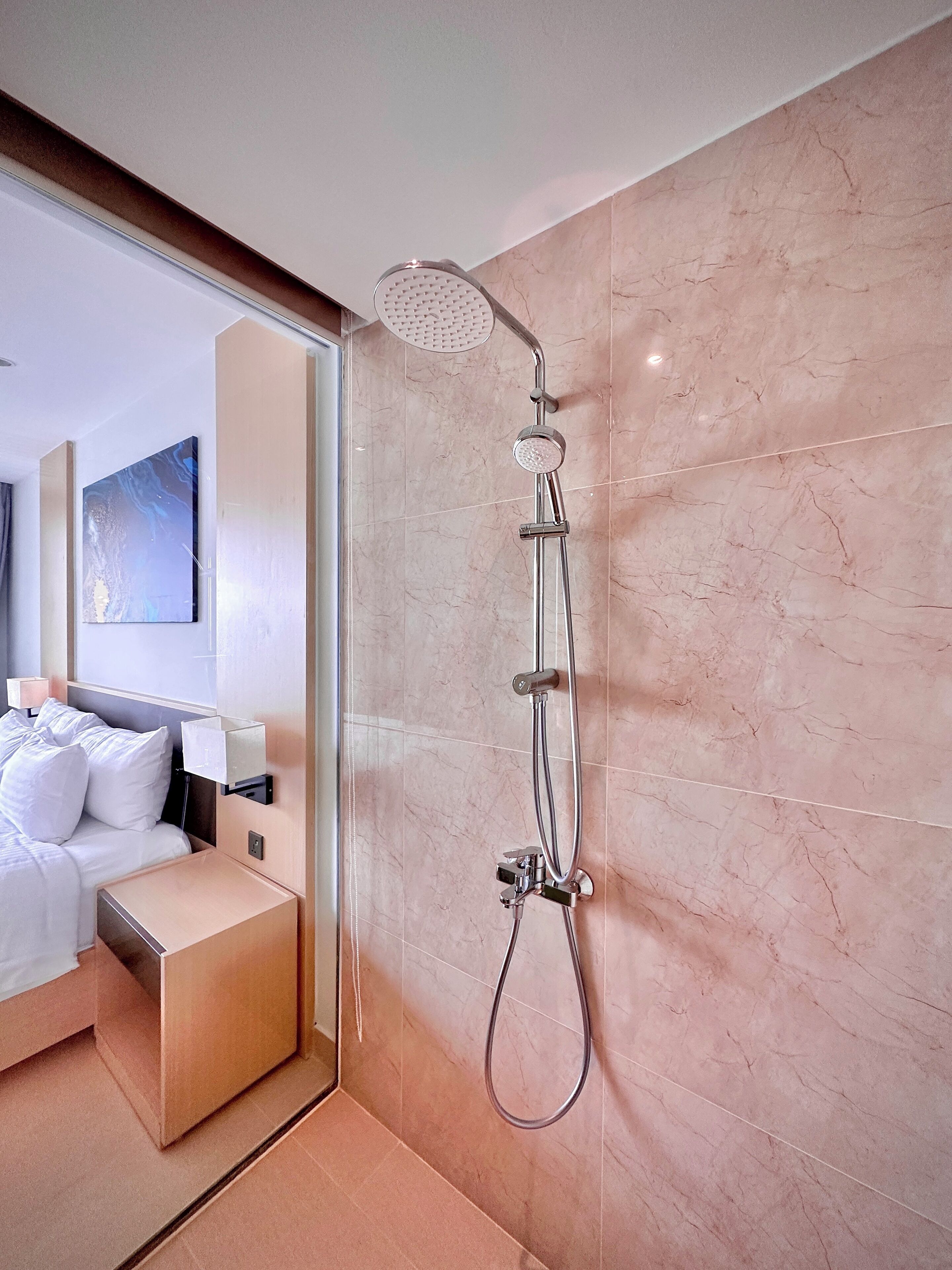 A modern bathroom with a shower, marble walls, a bed, and a bedside table.