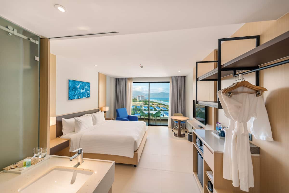 A hotel room with a large bed, a desk, a television, and a view of a cityscape.