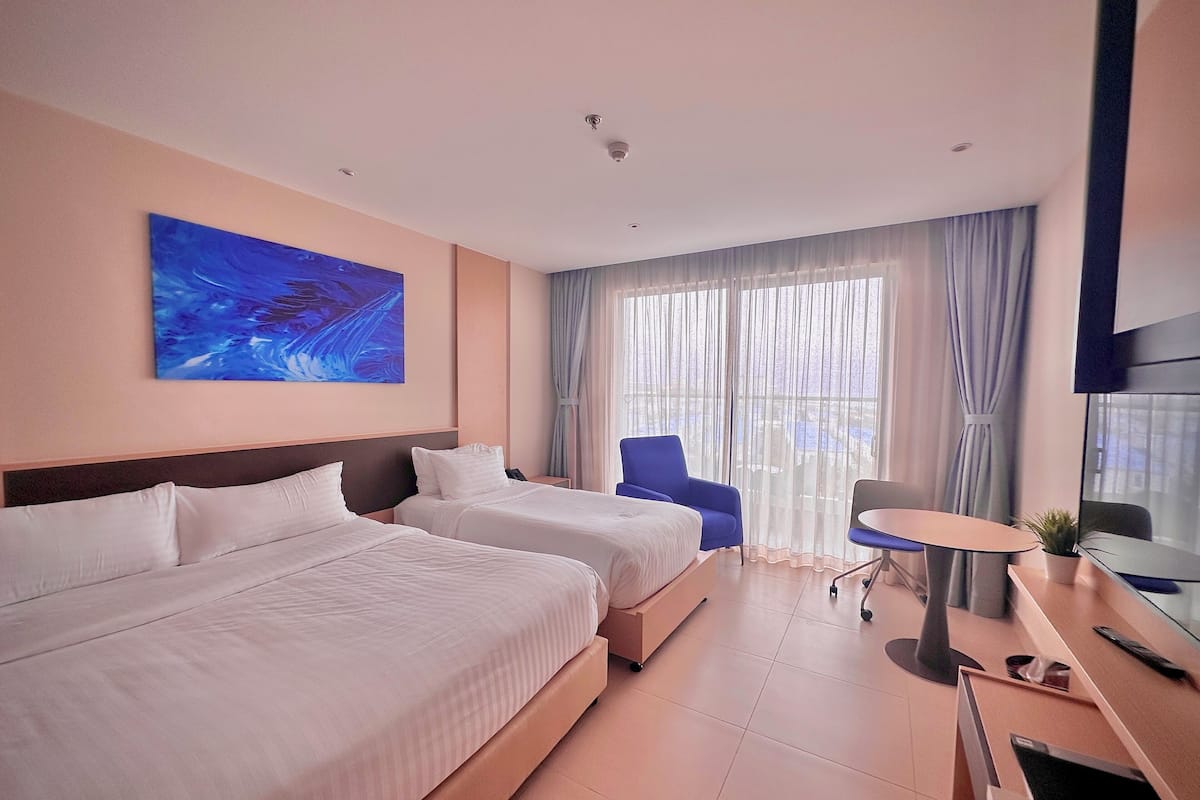 A hotel room with two beds, a desk, a chair, and a large window with curtains.