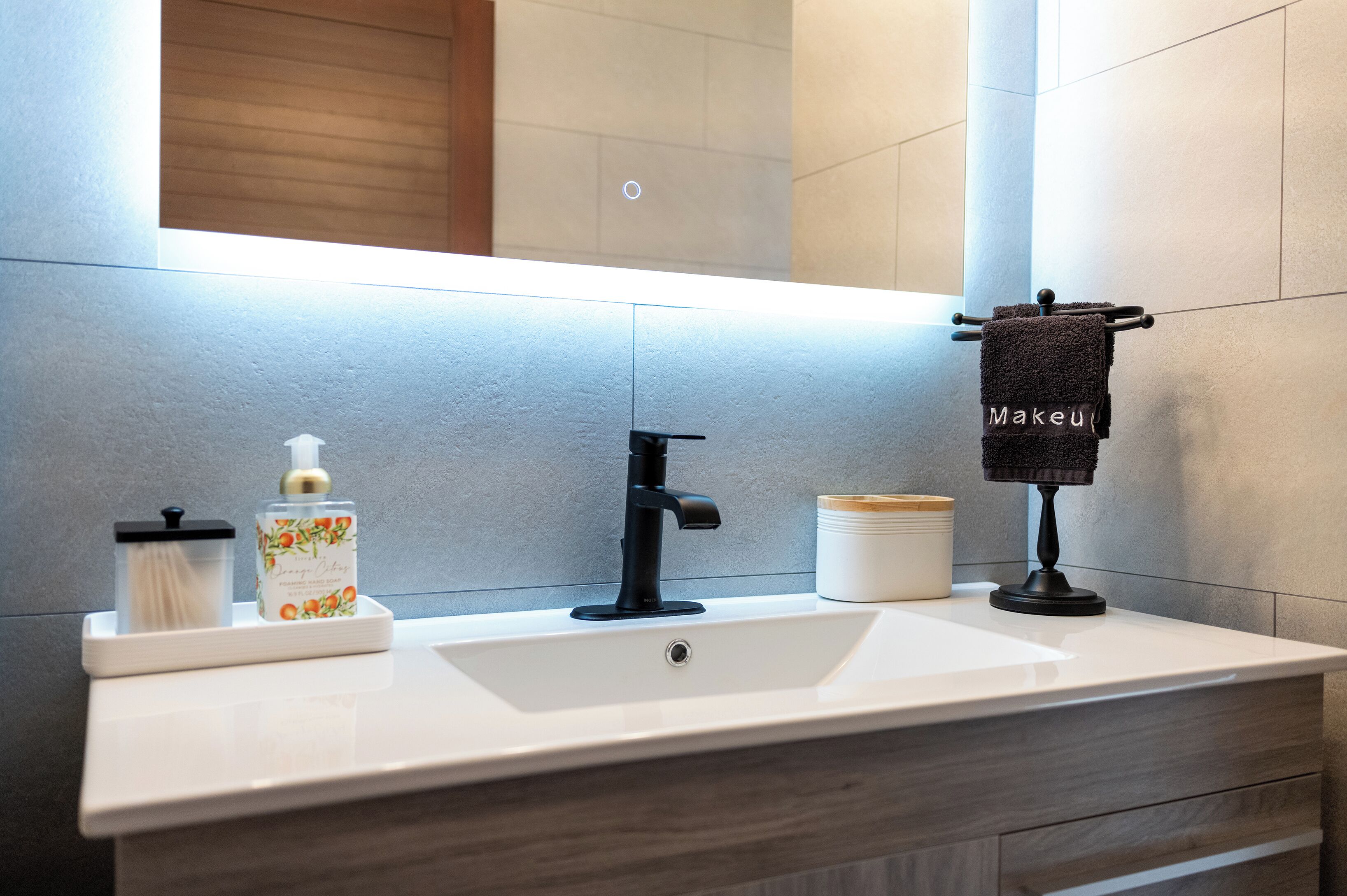 A modern bathroom with a white sink, black faucet, and a towel rack with a towel labeled "Makeup".