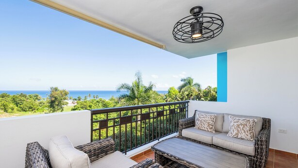 A balcony with wicker furniture, a view of the ocean, and a blue accent wall.