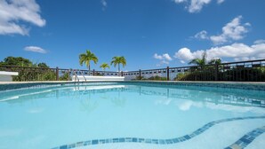 A clear blue swimming pool with a tiled edge, surrounded by a wooden fence and palm trees.