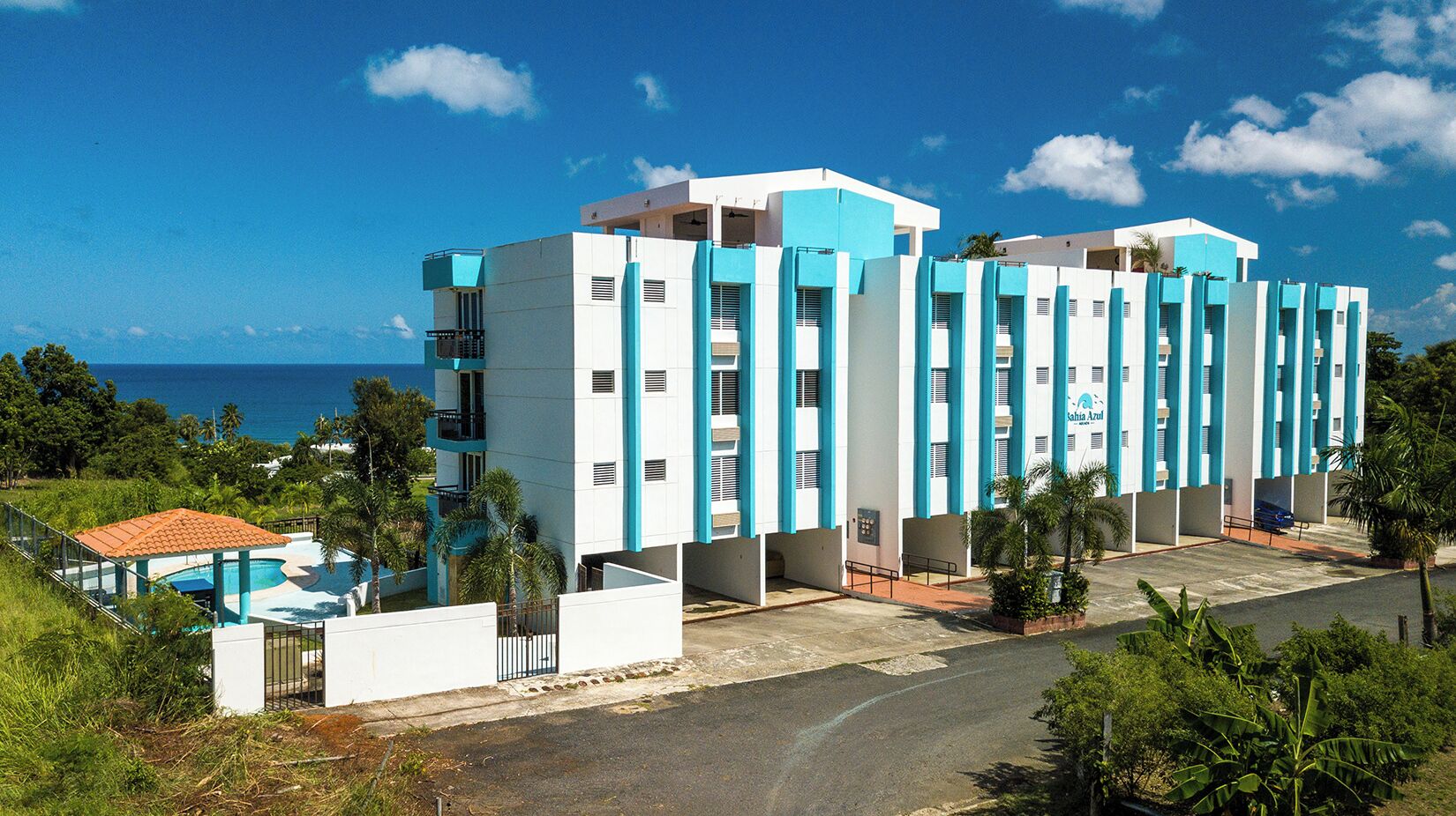 A modern hotel with a pool, multiple floors, and a view of the ocean.