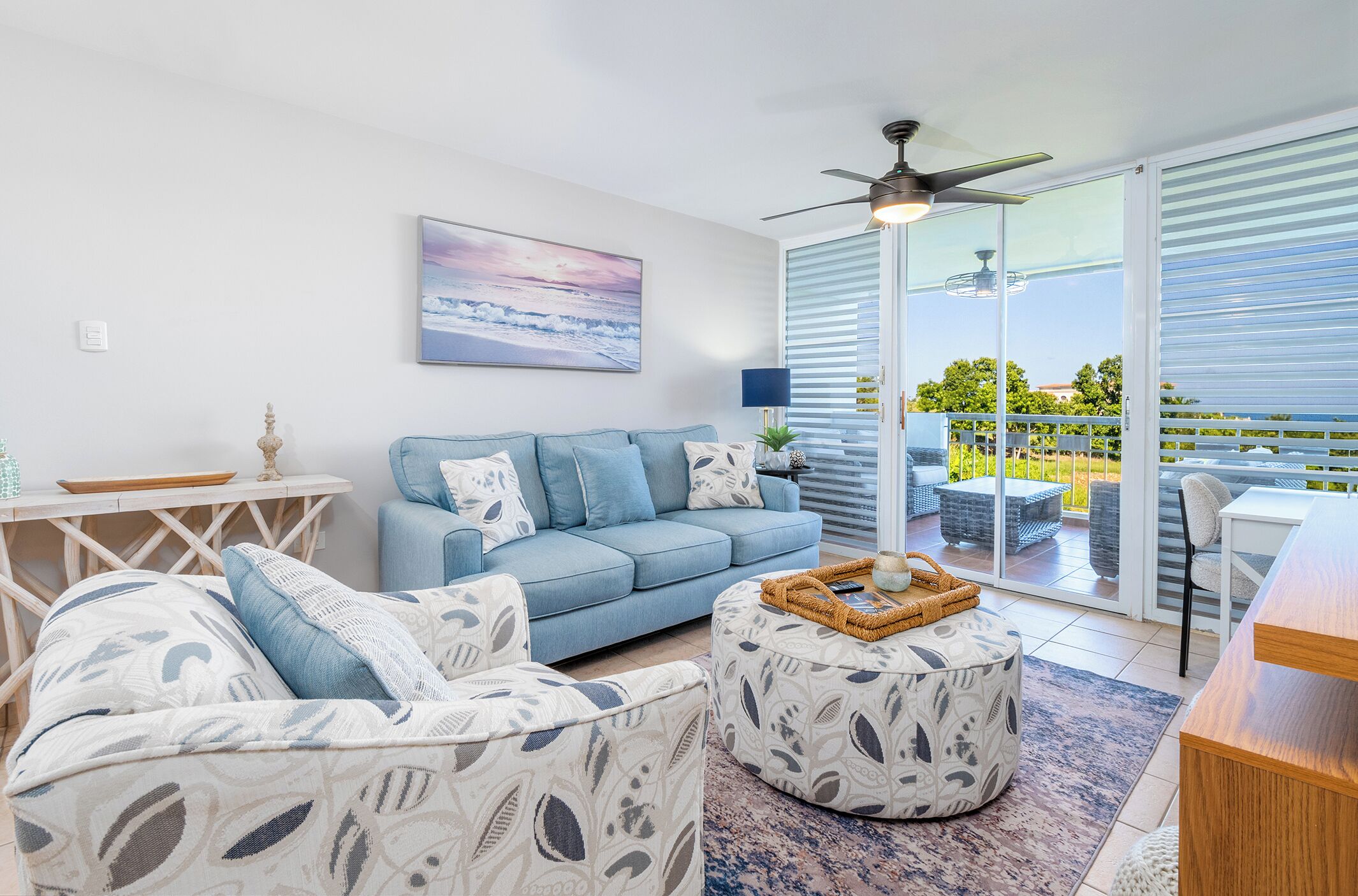 A modern living room with a blue sofa, patterned ottoman, and a dining area with a table and chairs.