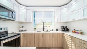 A modern kitchen with white cabinets, a black stove, and a window with blinds.