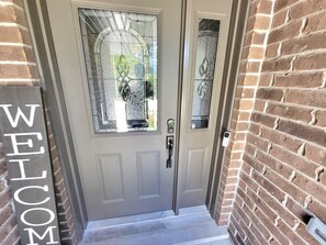 A front door with a 'WELCOME' sign, a glass door with a decorative pattern, and a brick wall.
