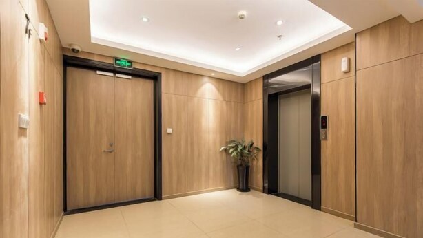 Un hall d’ascenseur moderne avec un lambris en bois, une plante en pot et un panneau indiquant clairement la sortie de secours.