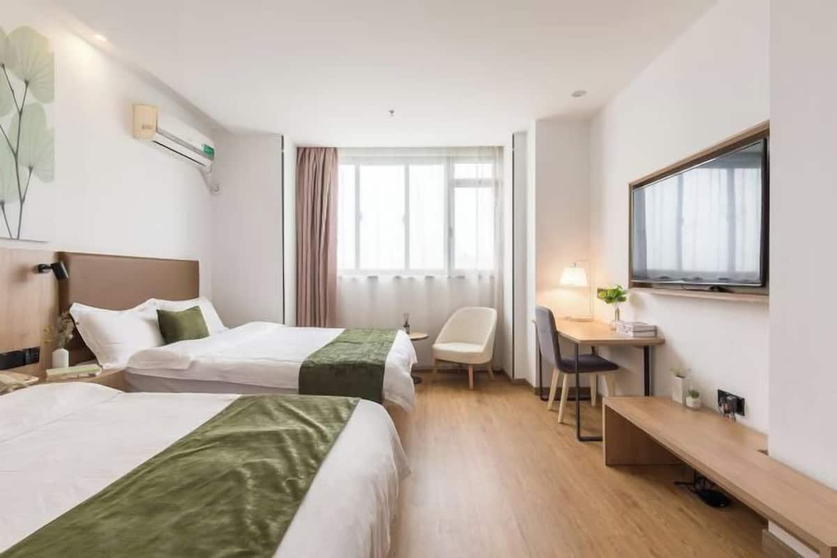 A hotel room with two beds, a desk, a chair, a TV, and a window with curtains.