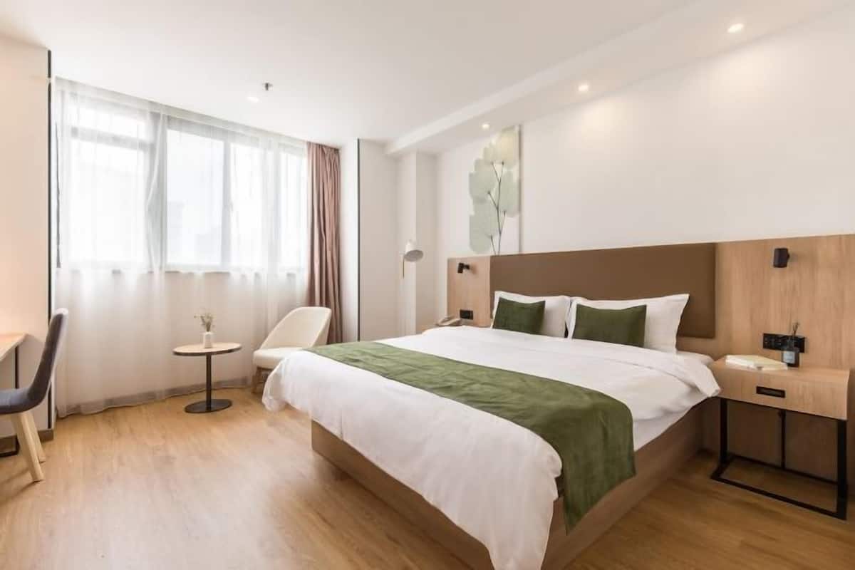 A modern hotel room with a large bed, a small round table, a chair, and a nightstand.