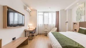 Ett hotellrum med en säng, ett skrivbord, en stol, en tv och ett litet bord.