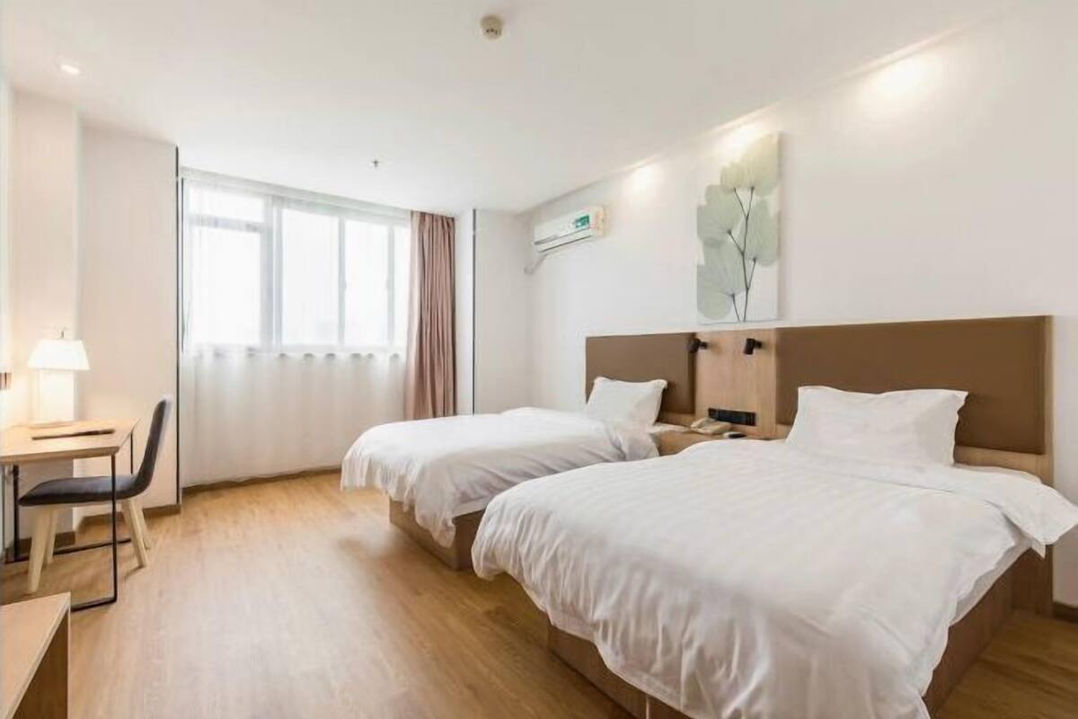 A hotel room with two beds, a desk, a chair, and a window with curtains.