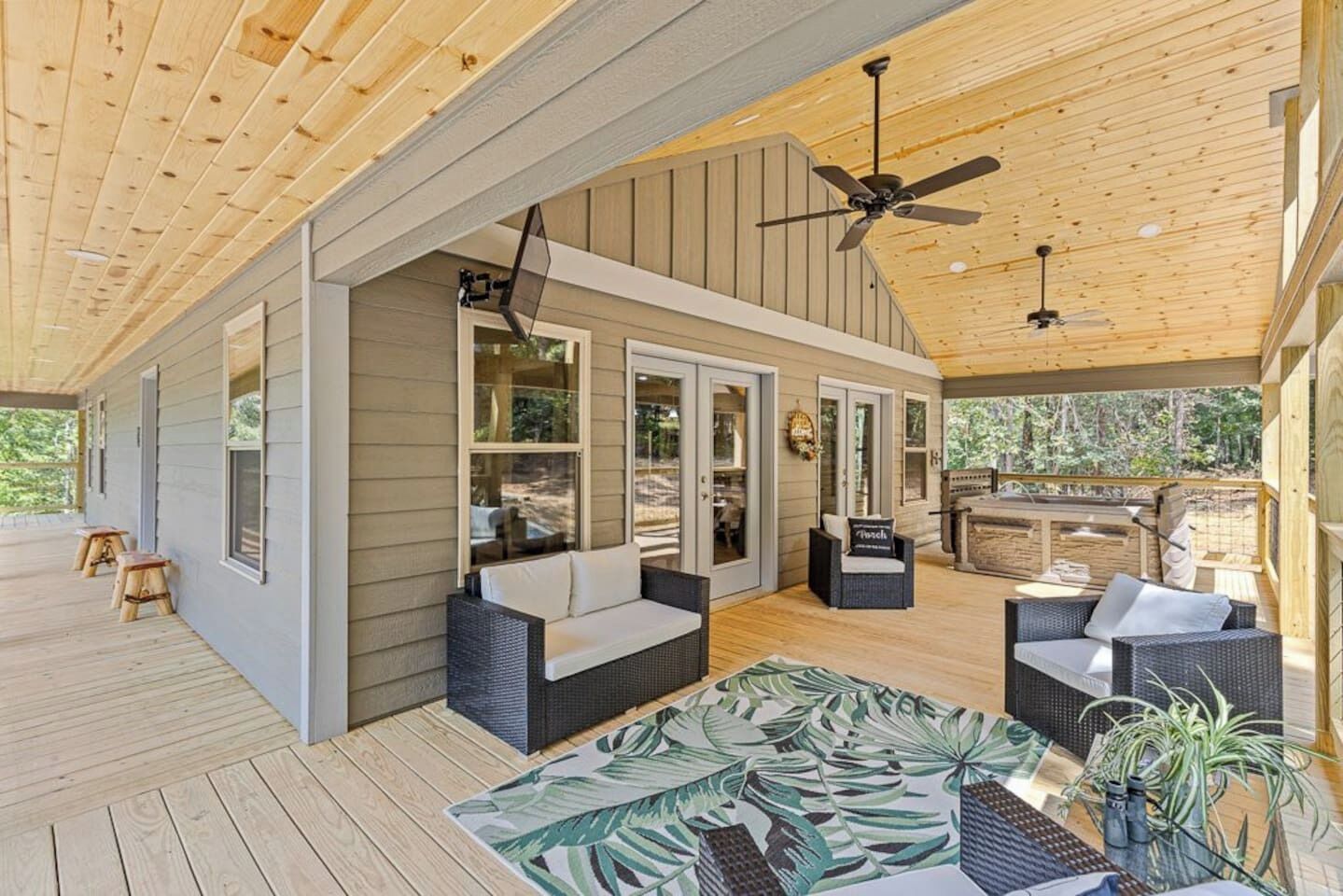 A covered outdoor area with wooden flooring, wicker furniture, and ceiling fans.