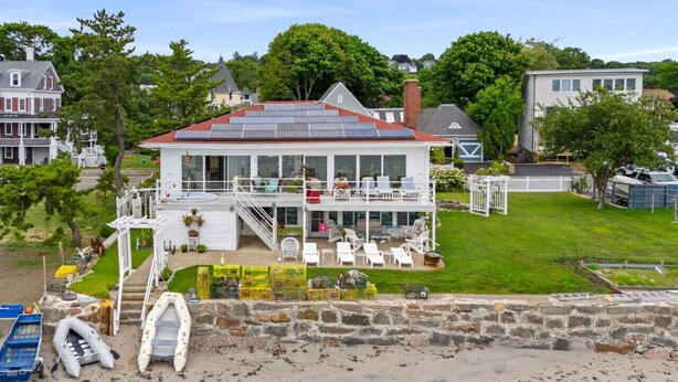 A coastal house with a large balcony, a covered outdoor seating area, and a view of the beach.