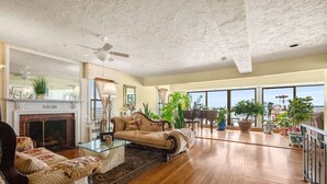 A spacious living room with a fireplace, a large window with a view, and a piano.