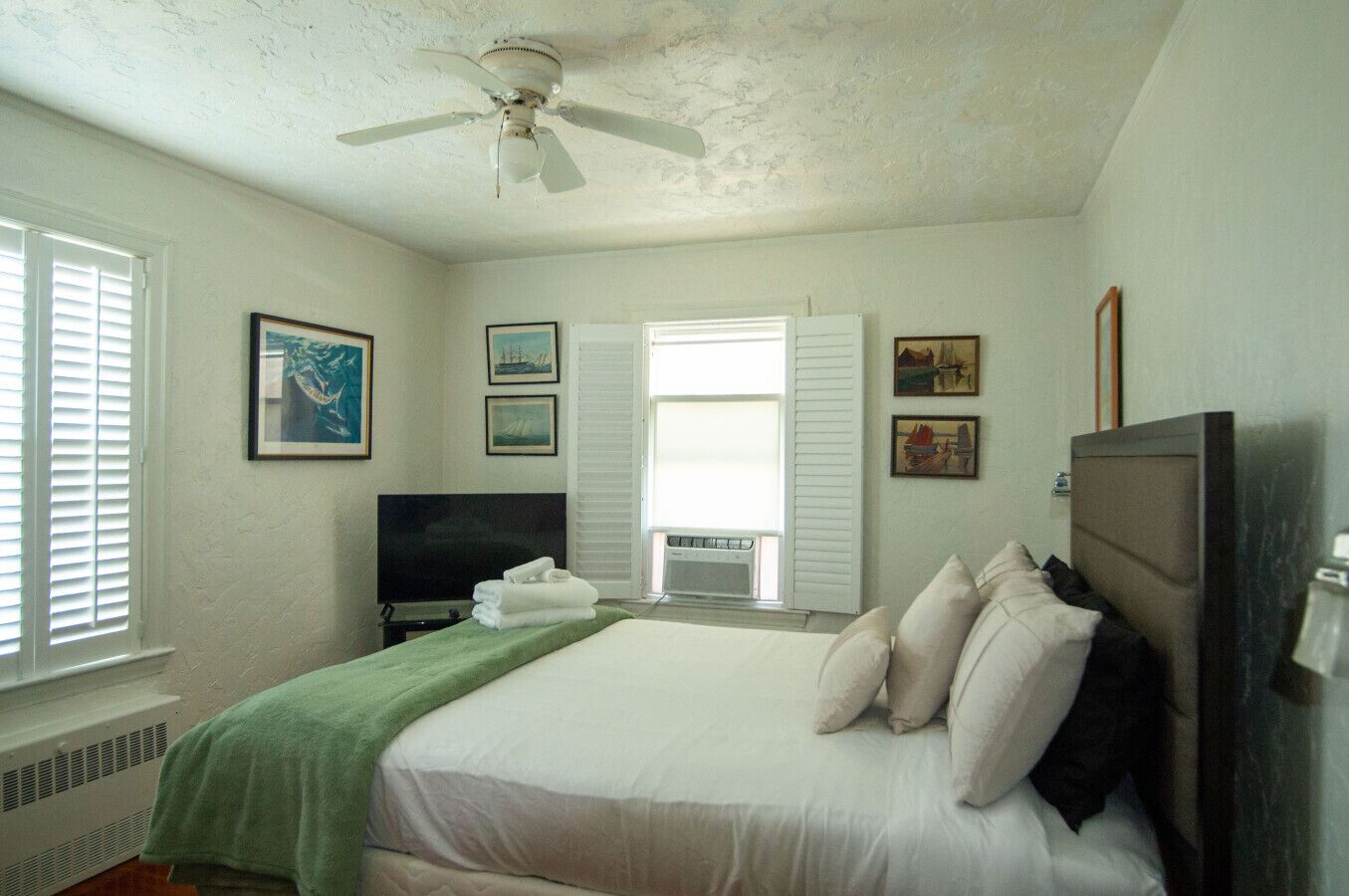 Ein Schlafzimmer mit Bett, Fernseher, Deckenventilator und Kunstwerken an den Wänden.
