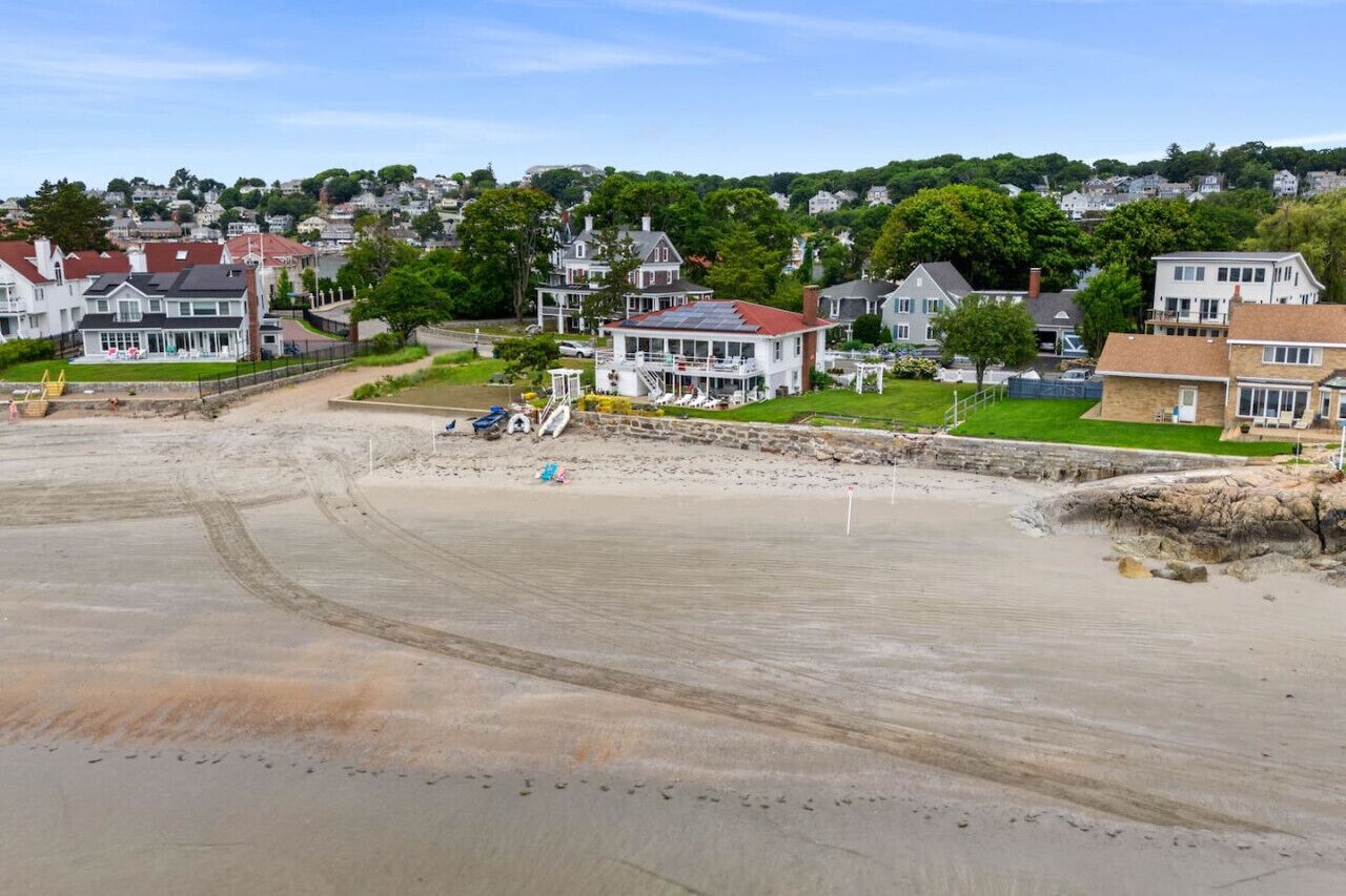 A coastal residential area with houses, a sandy beach, and a rocky shoreline.