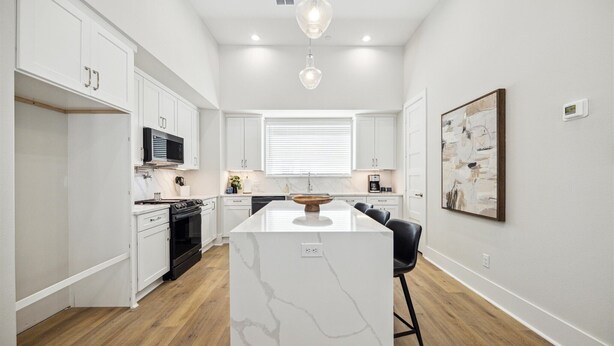 A modern kitchen with white cabinetry, a marble island, and a wooden floor. - Luxury Group Retreat | Rooftop Deck + Chef's Kitchen | Sleeps 10 (Houston)