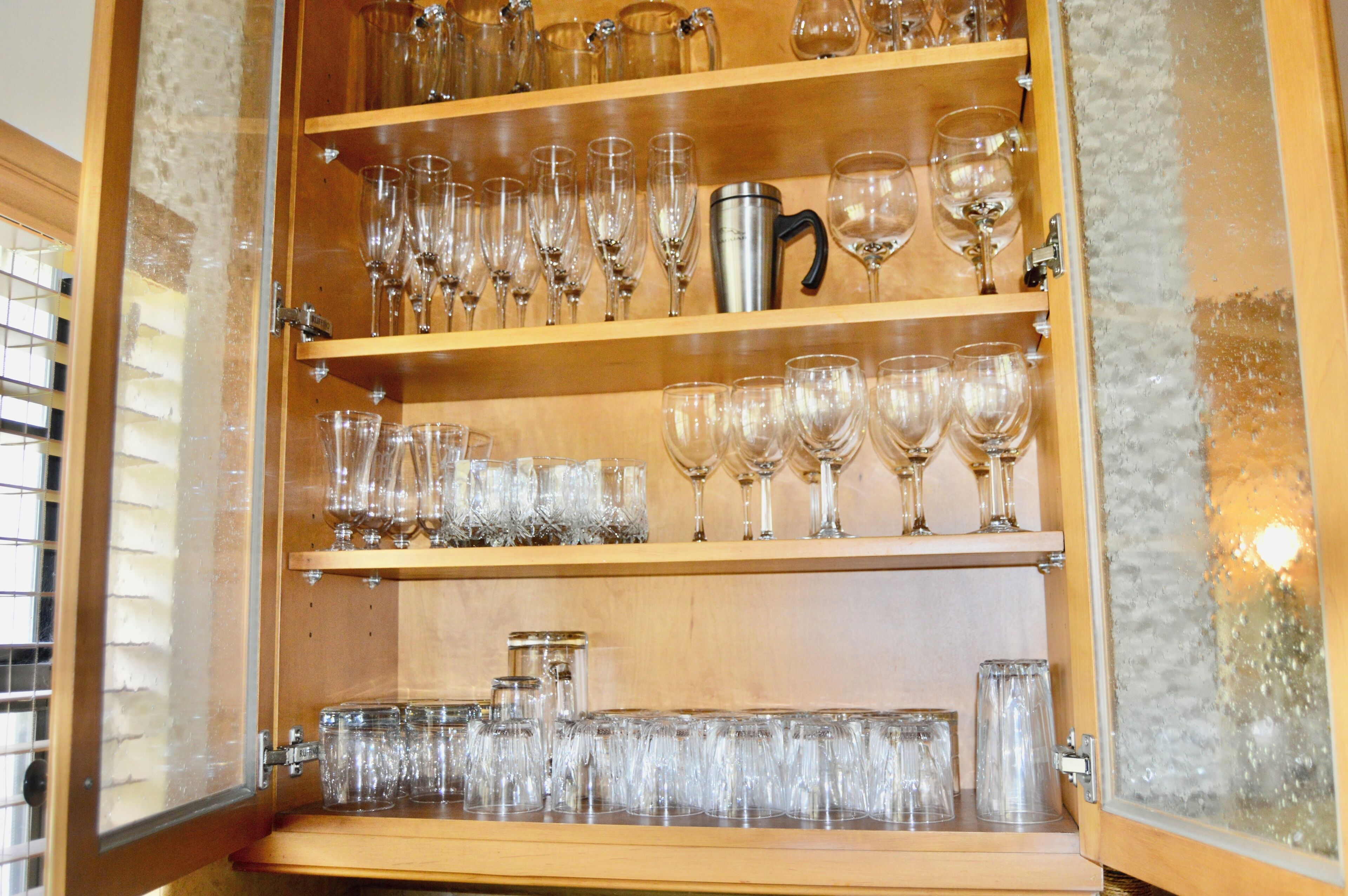 A wooden cabinet with multiple shelves containing various glassware, including wine glasses and tumblers.