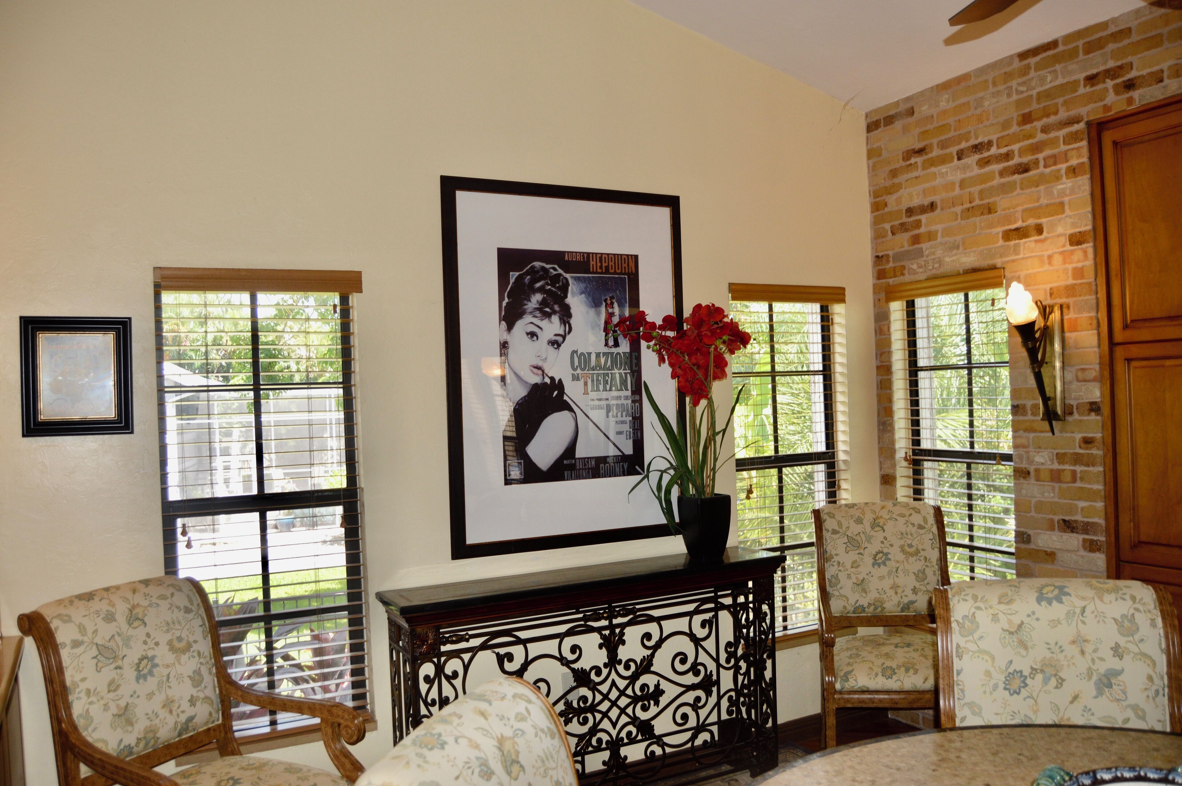 A room with two upholstered chairs, a console table with a framed picture, and a potted plant.