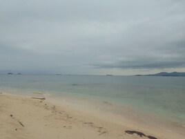 Una playa con agua cristalina y formaciones terrestres a lo lejos.