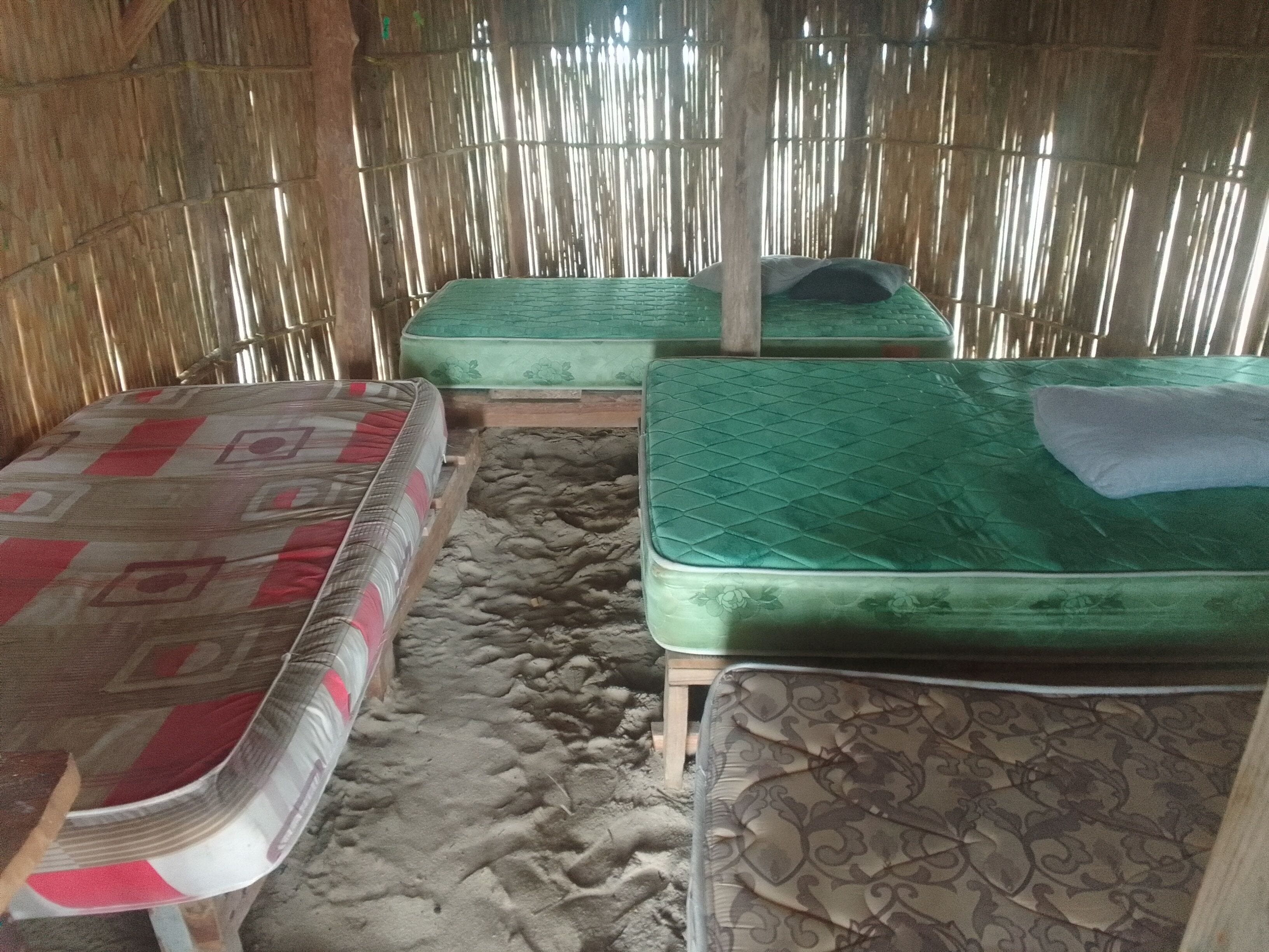 A room with two mattresses on the floor, a wooden table, and a bamboo wall.