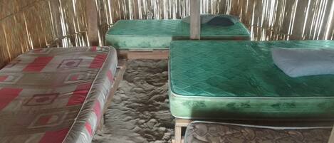 A room with two mattresses on the floor, a wooden table, and a bamboo wall.