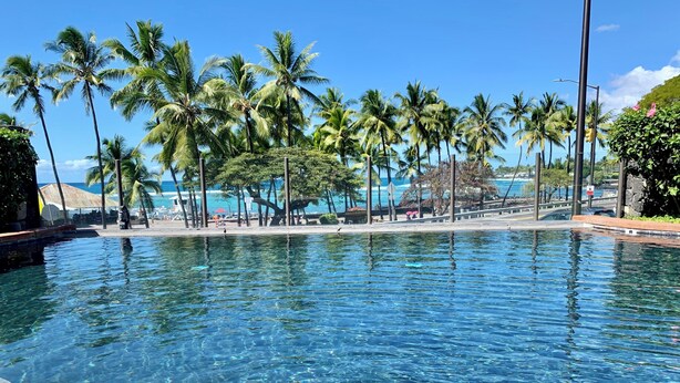 Une piscine aux eaux cristallines, avec vue sur des palmiers et une plage.