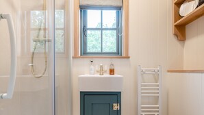 A bathroom with a glass shower enclosure, a sink with toiletries, a window, and a towel rack. - Set among the fruit trees with views of the fields. (Ongar)